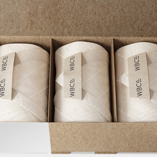 Three rolled bamboo cloths placed side by side in an open cardboard box, with the brand label 'WBCO' visible on each roll. face wipe