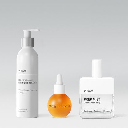 A set of three skincare products from WBCo, including a balancing cleanser in a white pump bottle, a glow oil in a round dropper bottle, and a prep mist in a spray bottle. facial spray is coconut.