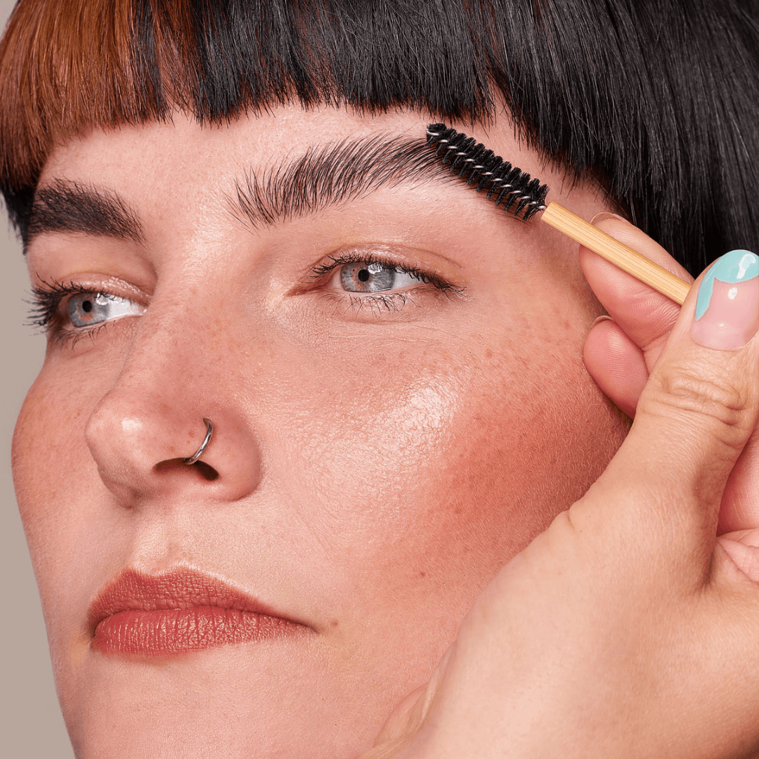 A single bamboo spoolie brush brushing an eyebrow grooming the face for make up and brow grooming. 