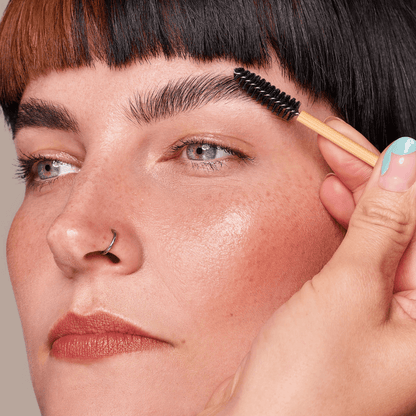 A single bamboo spoolie brush brushing an eyebrow grooming the face for make up and brow grooming. 